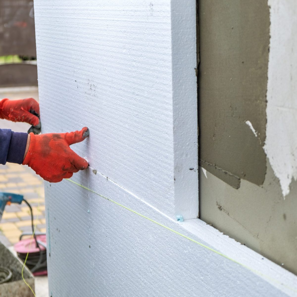 Construction worker installing styrofoam insulation sheets on house facade wall for thermal protection.